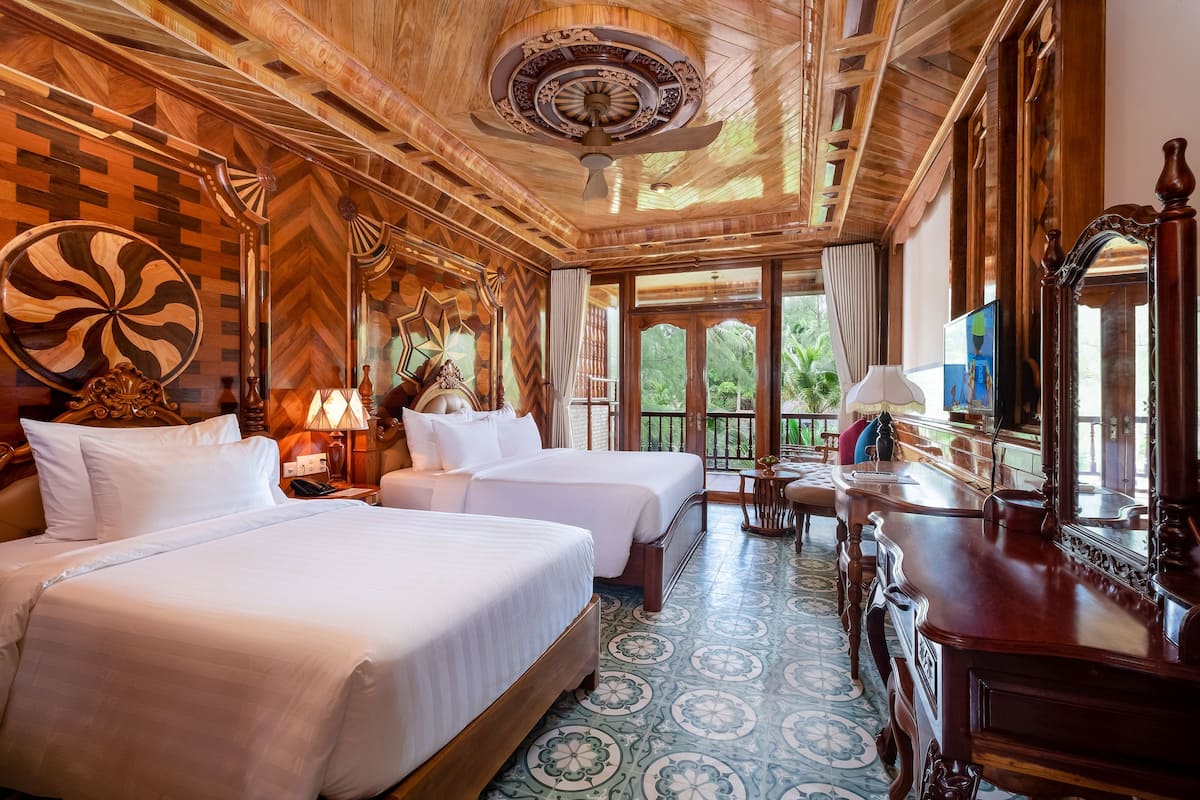 A hotel room with two beds, a wooden ceiling, a large mirror, and a view of greenery outside.