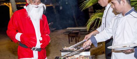 A person in a Santa costume standing next to a grill with food being cooked.