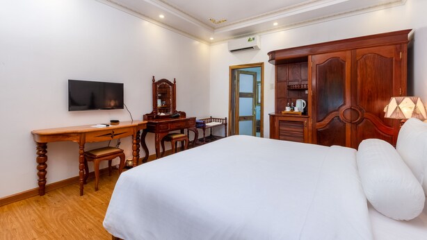 A hotel room with a large bed, wooden desk, television, and wardrobe. - Coco Palm Beach Resort & Spa (Phu Quoc)