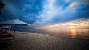A beach with a clear sky, a person walking, and a beach umbrella. - Cassia Cottage Resort and Spa (Phu Quoc)
