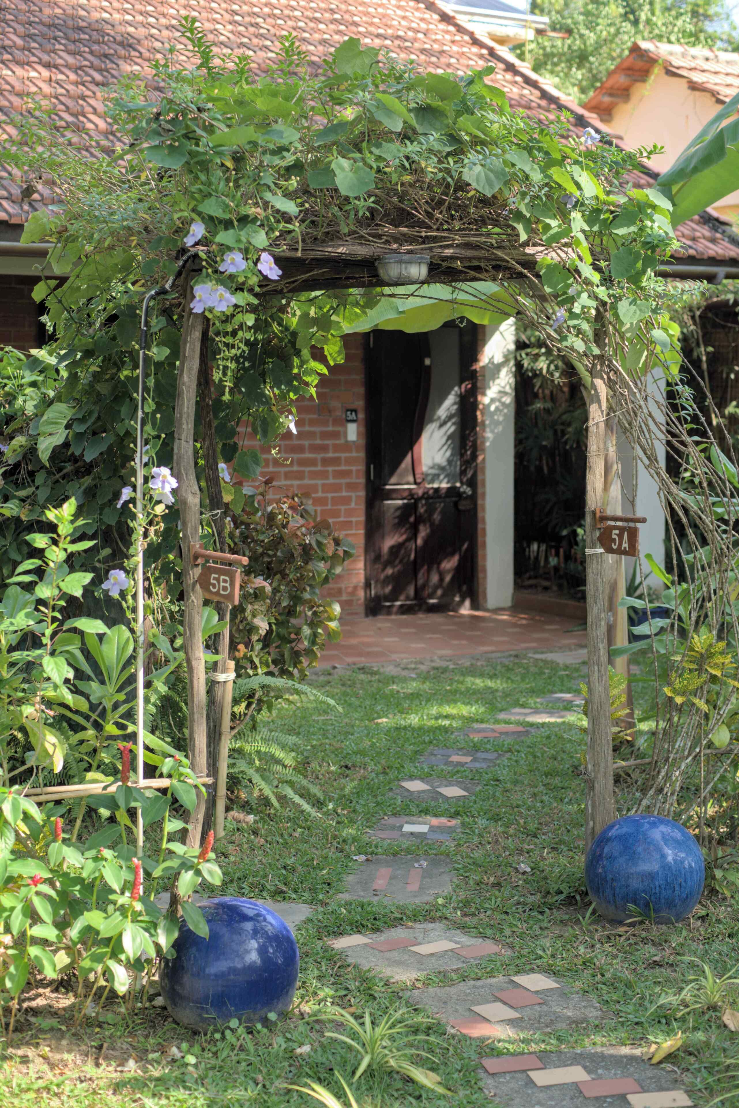 A garden entrance with a wooden archway, a brick pathway, and a blue spherical object.