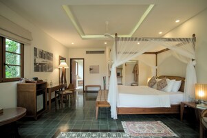 A bedroom with a four-poster bed, a desk with a chair, a television, and a window.