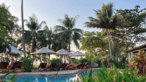 A pool area with lounge chairs and umbrellas, surrounded by palm trees and tropical plants. - Cassia Cottage Resort and Spa (Phu Quoc)