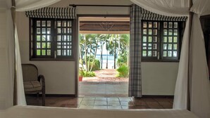 A room with a view of a beach and palm trees, a chair, and a bed. - Cassia Cottage Resort and Spa (Phu Quoc)