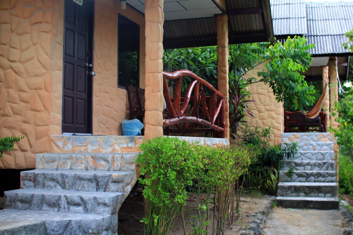 A building with stone steps leading to a door, surrounded by greenery and a hammock.