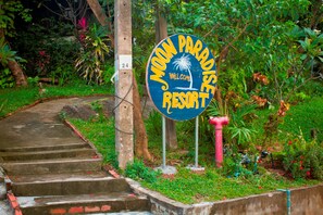 A sign for Moon Paradise Resort with a palm tree and waterfall design, surrounded by lush greenery and a concrete pathway.