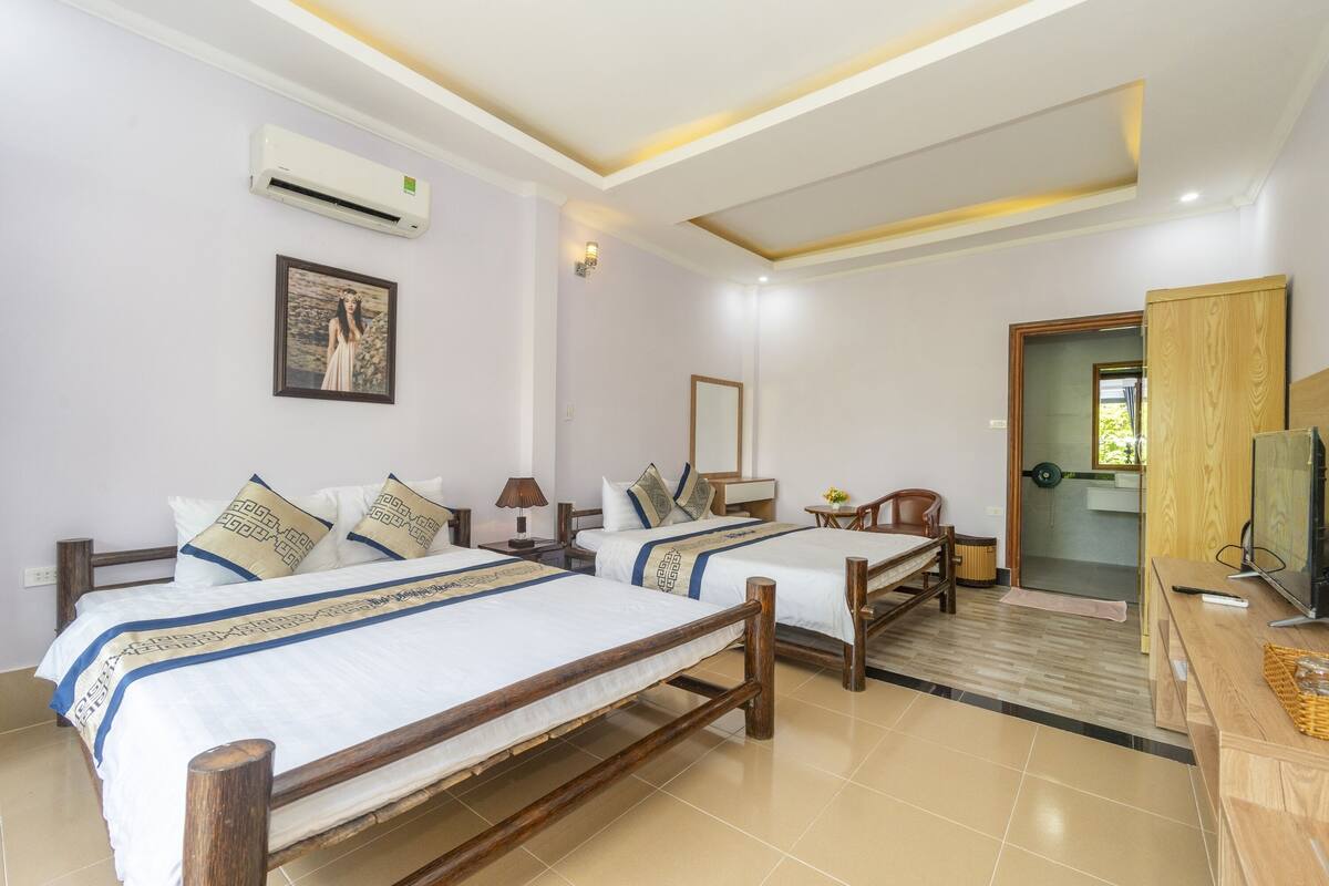 A hotel room with two wooden beds, a TV, a desk, and a bathroom visible through an open door.