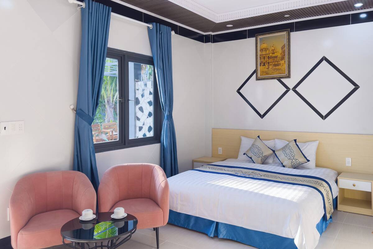 A hotel room with a bed, two chairs, a small table, and a window with curtains.
