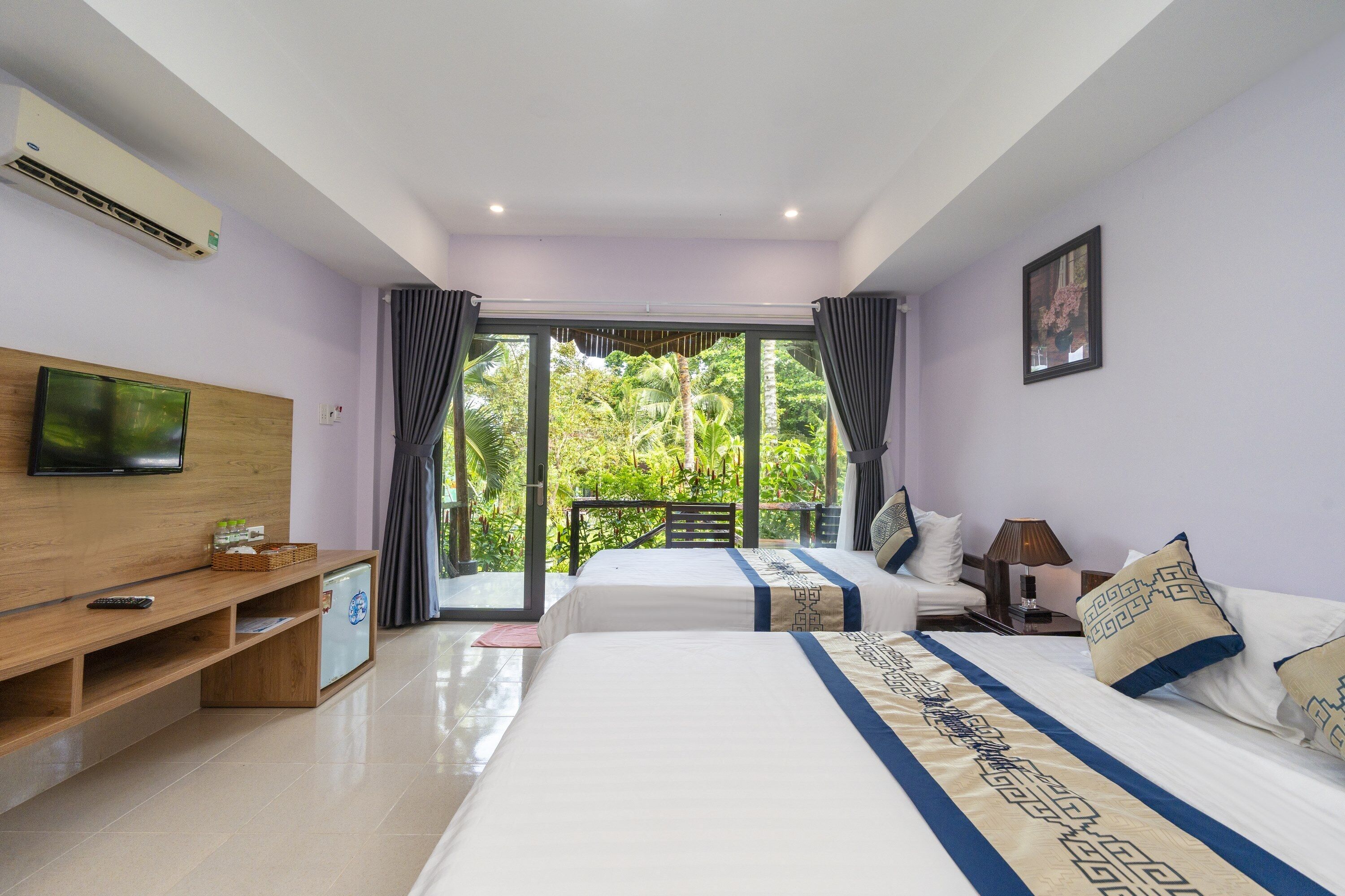 A hotel room with two beds, a TV, a wooden shelf, and a balcony with a view of greenery.