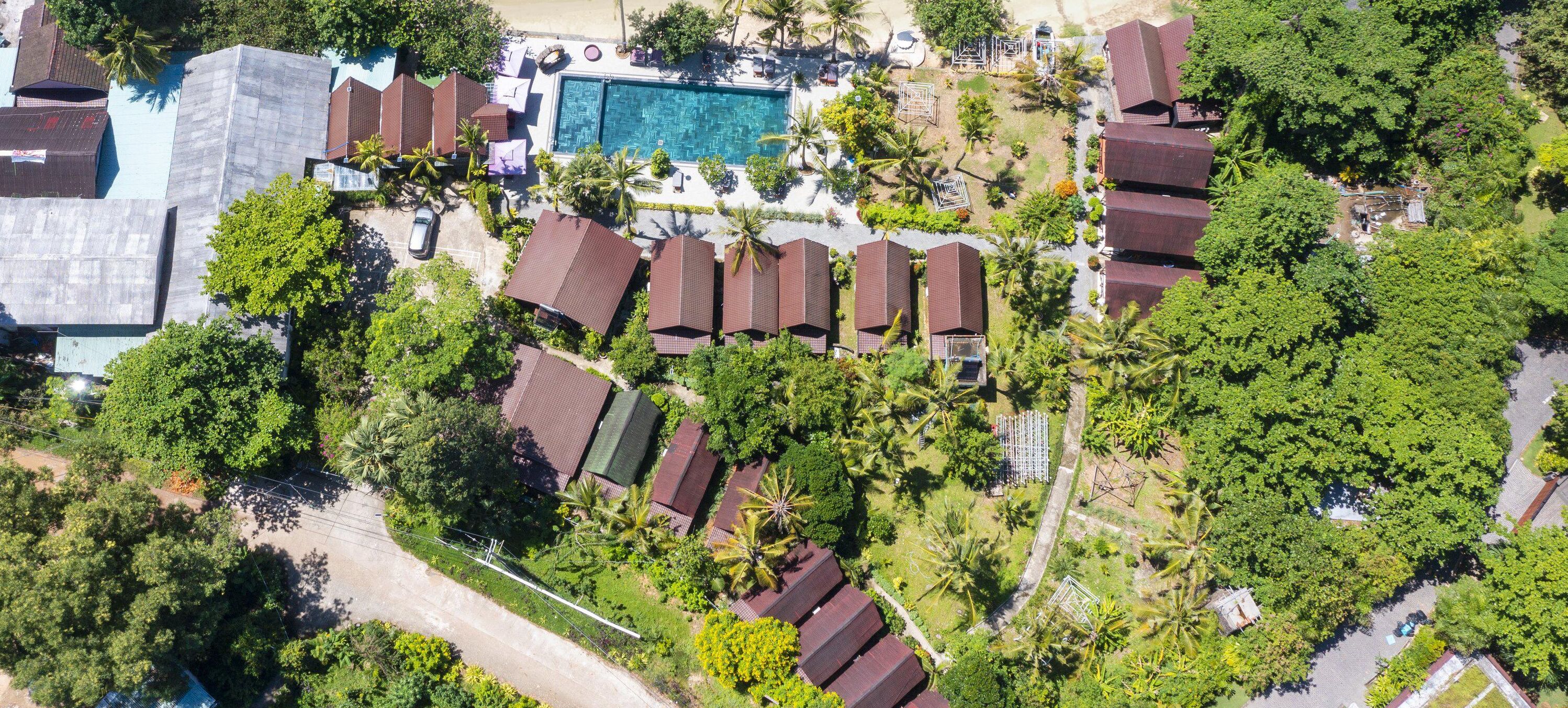 Vista aérea de un complejo turístico con varias cabañas, una piscina central y exuberante vegetación circundante.