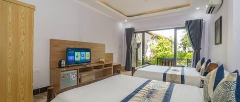 A hotel room with two beds, a TV, a minibar, and a balcony with a view of greenery.