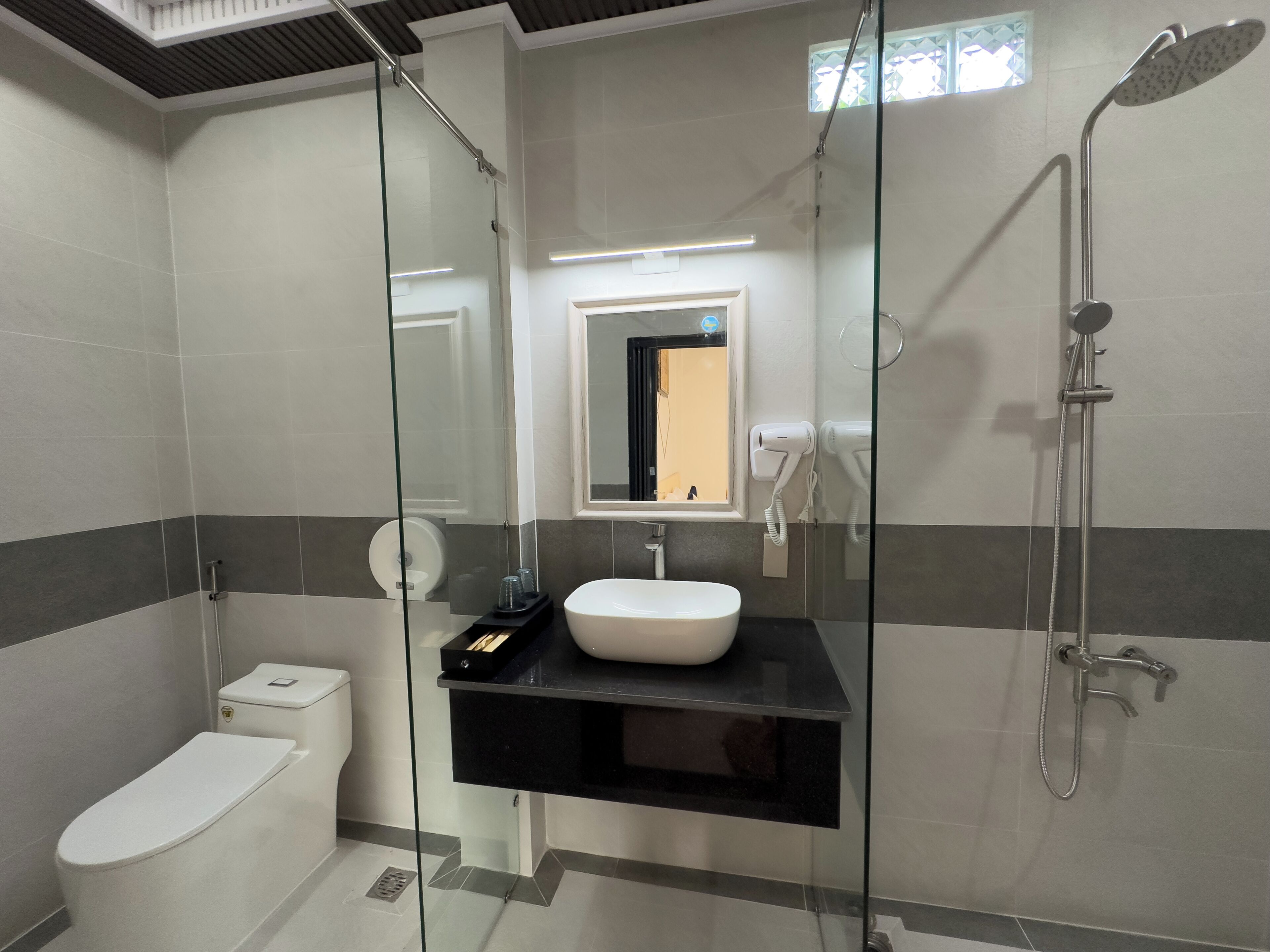 Ein modernes Badezimmer mit einer gläsernen Duschkabine, einer weißen Toilette und einem schwarzen Waschtisch mit Becken.