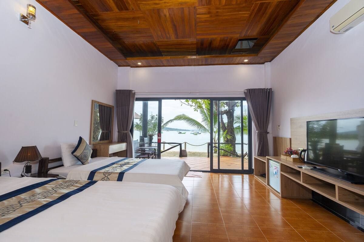 A hotel room with two beds, a TV, and a view of the beach.