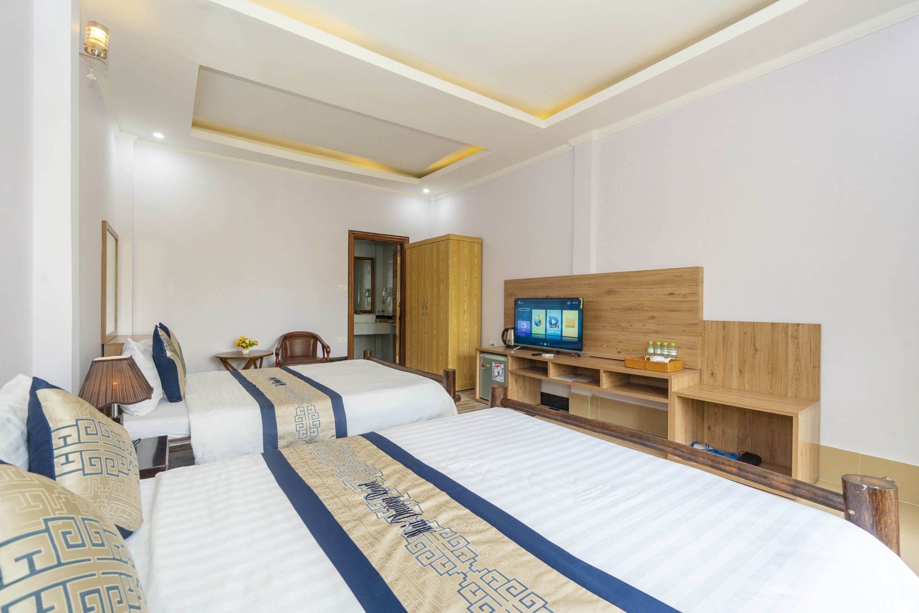 A hotel room with two beds, a TV, a wooden cabinet, and a desk with a lamp.