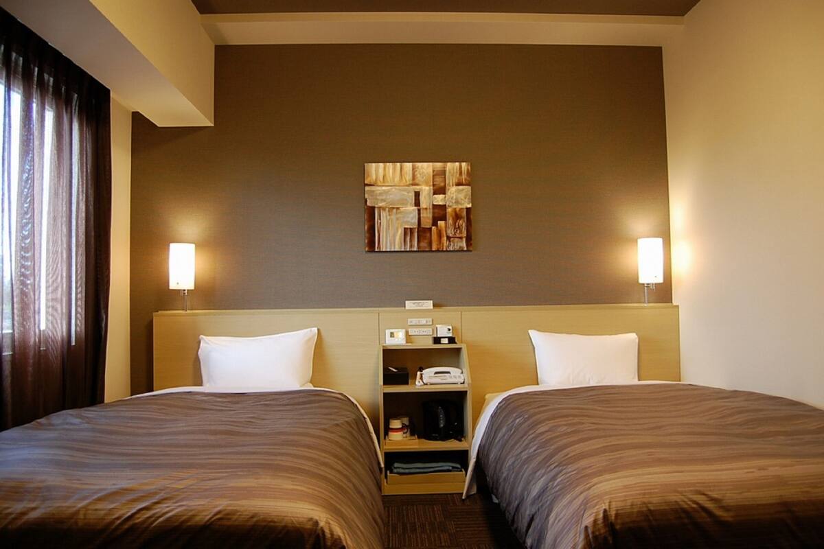 A hotel room with two beds, a headboard with a shelf, a wall-mounted artwork, and two bedside lamps.
