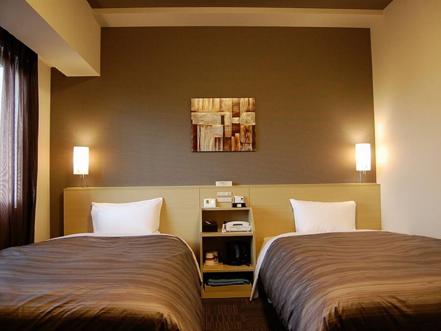 A hotel room with two beds, a headboard with a shelf, a wall-mounted artwork, and two bedside lamps.