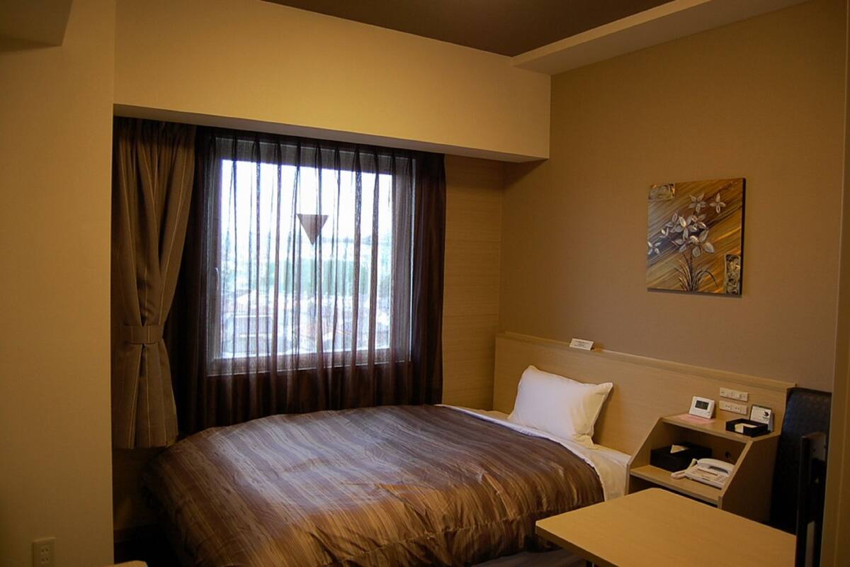 A hotel room with a large bed, a bedside table with a phone, and a window with curtains.