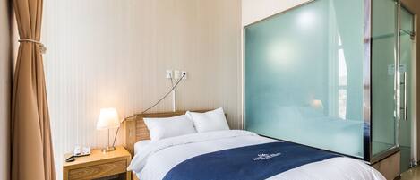Quarto de hotel com uma cama, mesa de cabeceira com abajur, guarda-roupa e cortina.