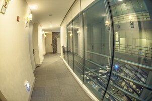 A corridor with glass walls, a tiled floor, and a staircase visible through the glass.