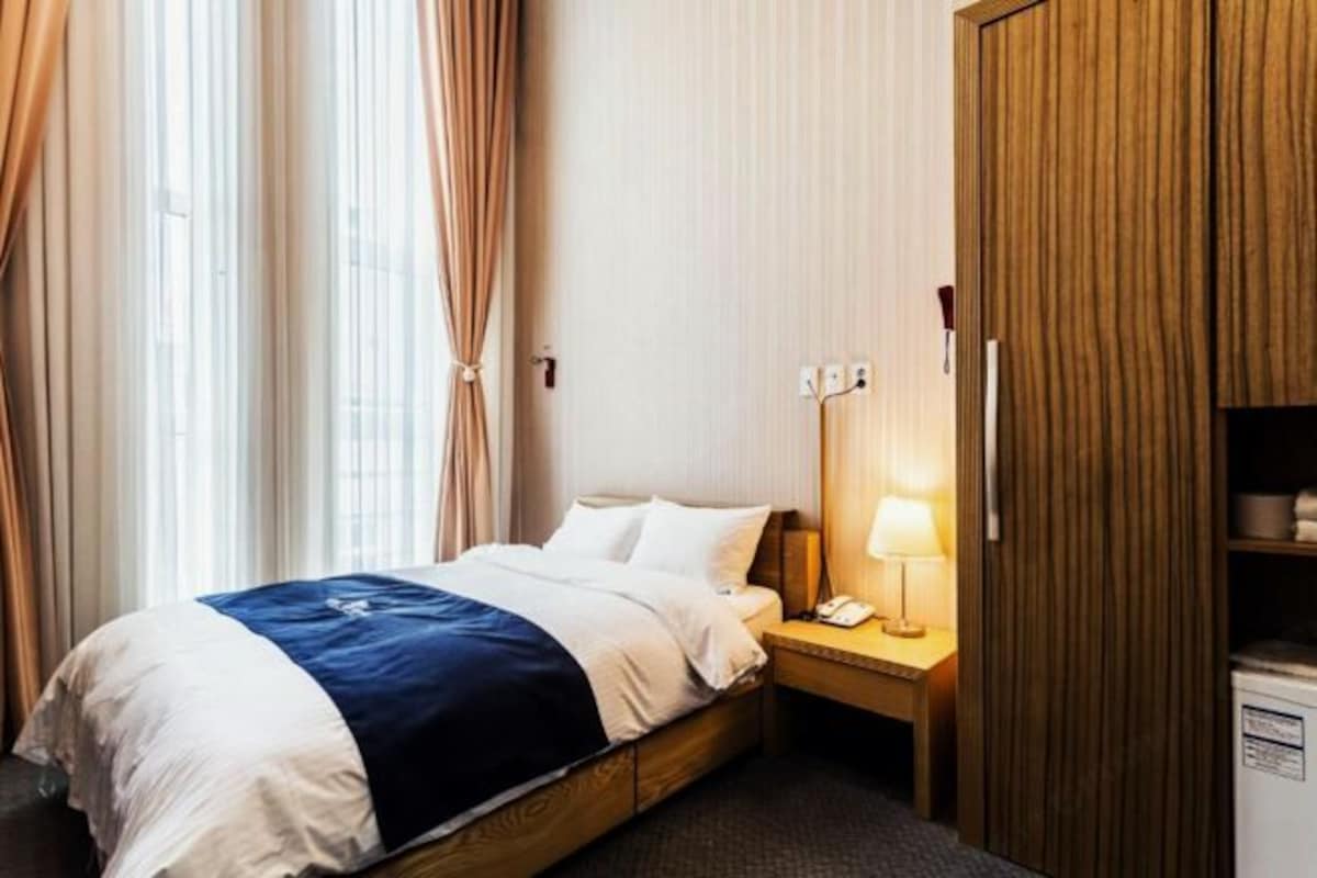 Habitación de hotel con cama, mesita de noche con lámpara, teléfono y armario.