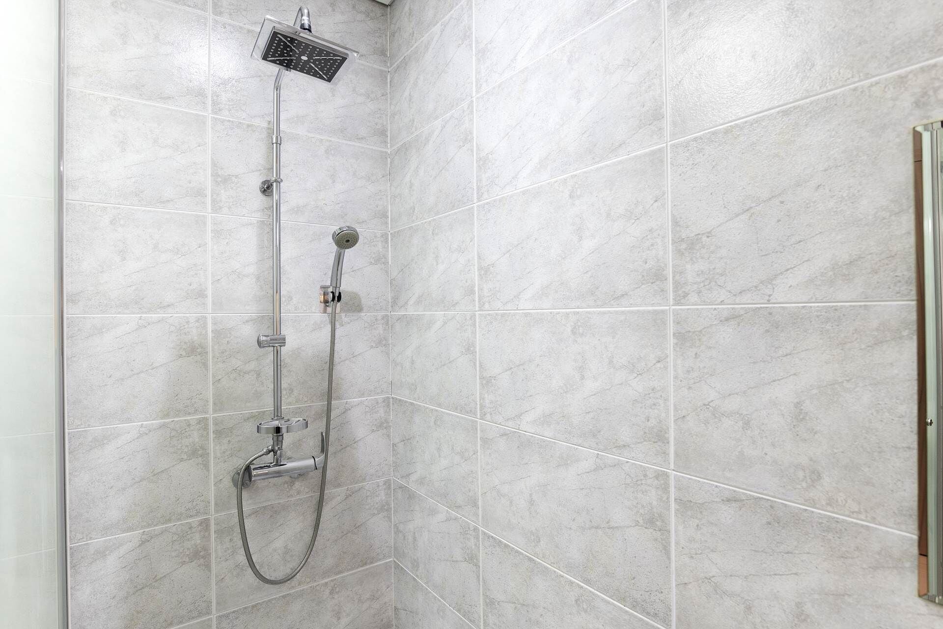 Une douche équipée d’un pommeau de douche à main et d’un pommeau de douche fixe fixé au mur, dans une salle de bain carrelée.
