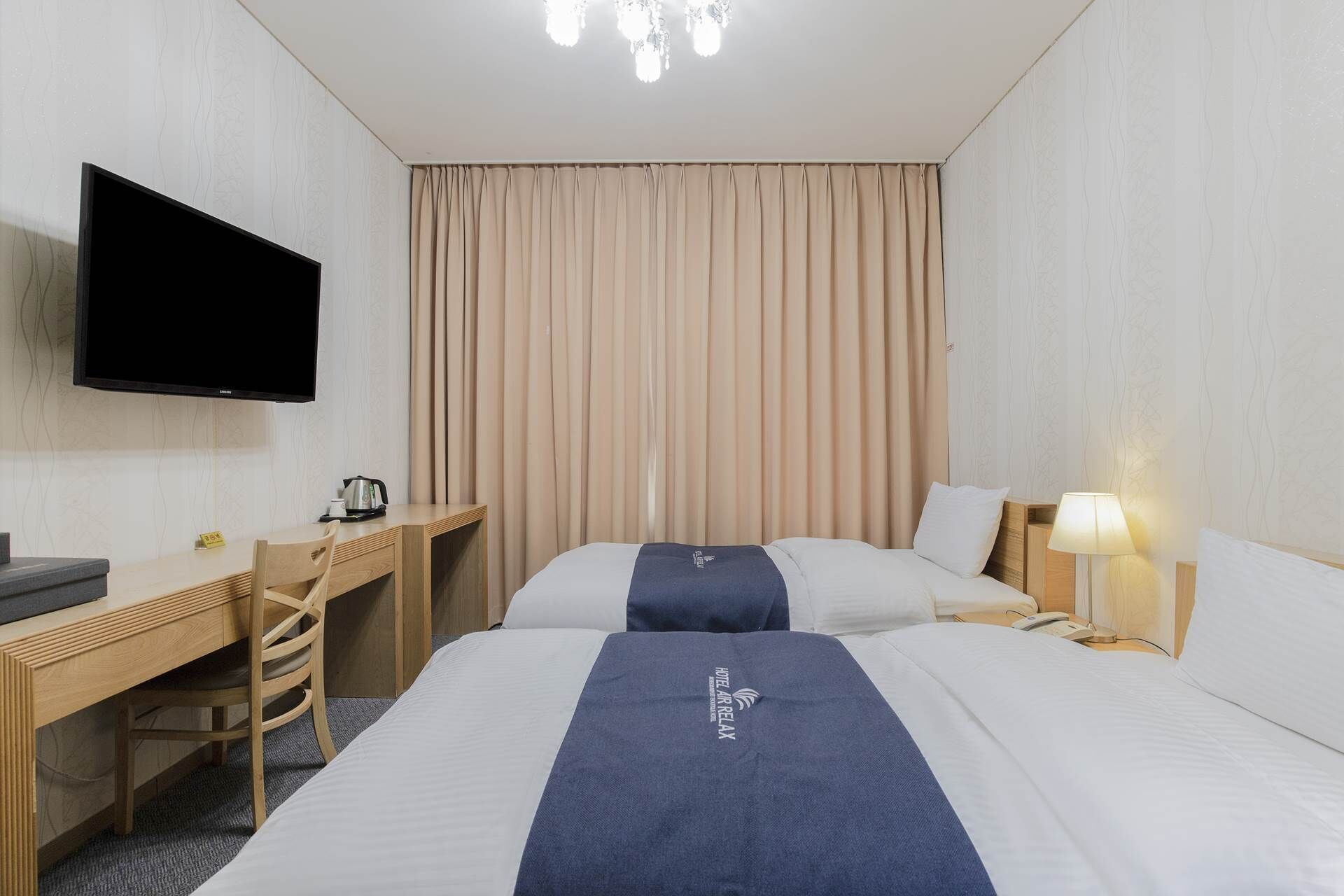 Una habitación de hotel con cama, escritorio, silla, televisor y lámpara.