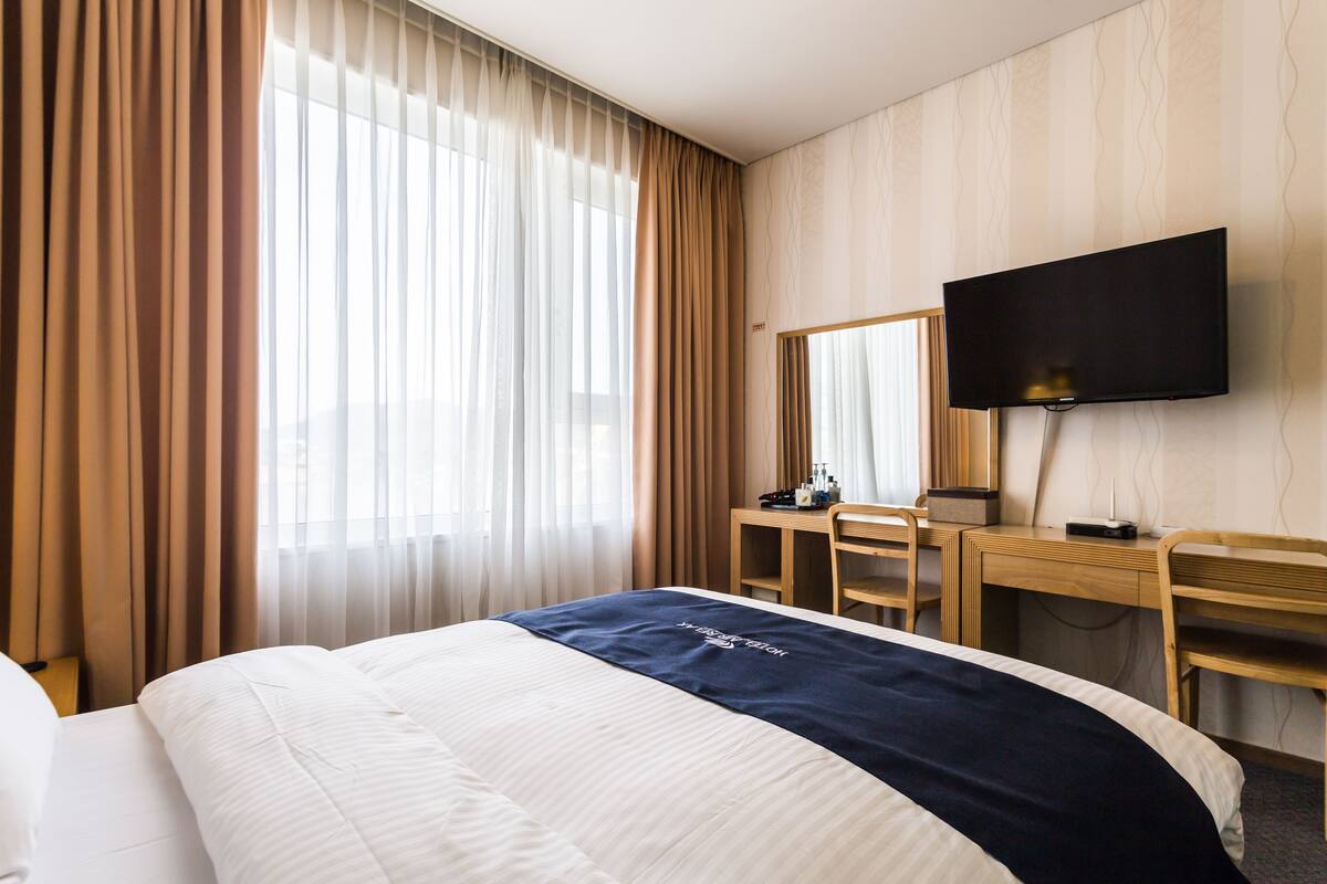 A hotel room with a bed, a desk, a chair, a television, and a window with curtains.