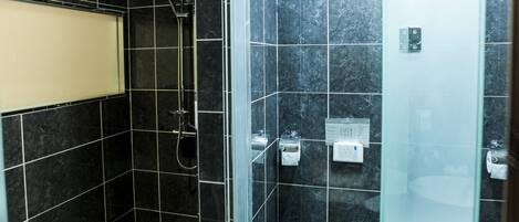 A modern bathroom with black marble tiles, a glass shower enclosure, and a white sink.