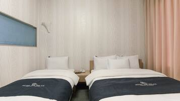 Ein Hotelzimmer mit zwei Betten, einem Nachttisch mit Telefon und einem Fenster mit Blick auf Blau.