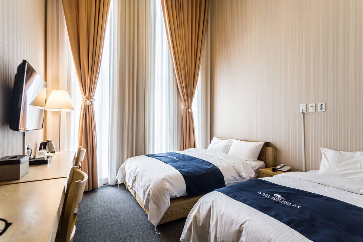 A hotel room with two beds, a desk, a lamp, a telephone, and a TV.