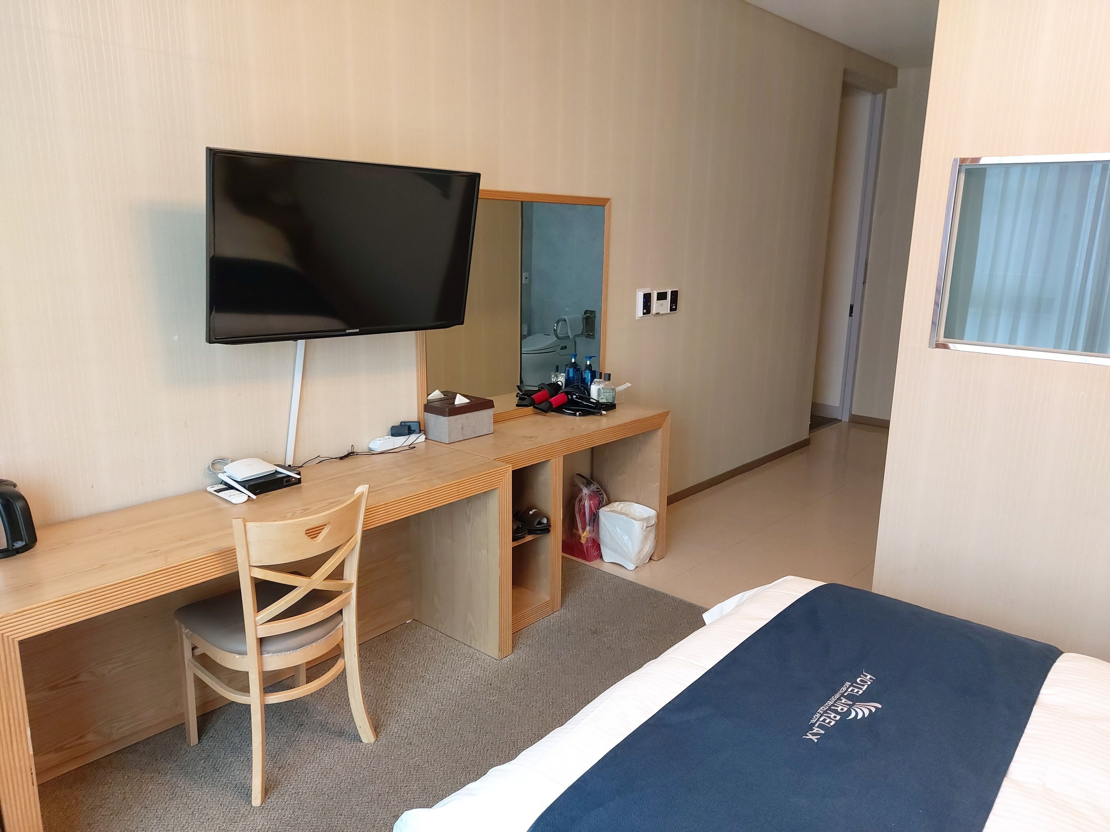 A hotel room with a wooden desk, a television, a bed with a blue cover, and a mirror.