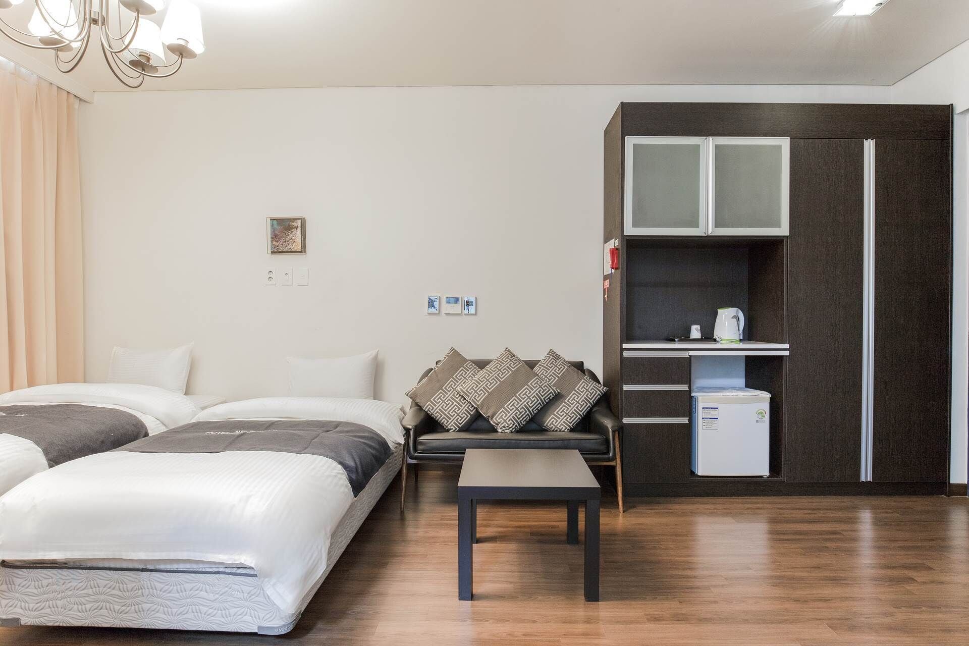 Hotelkamer met twee bedden, een klein tafeltje, een kitchenette met een koelkast en een donkerdrijgende garderobe.