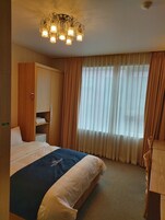 Une chambre d’hôtel avec un lit, une armoire, un bureau et un lustre.