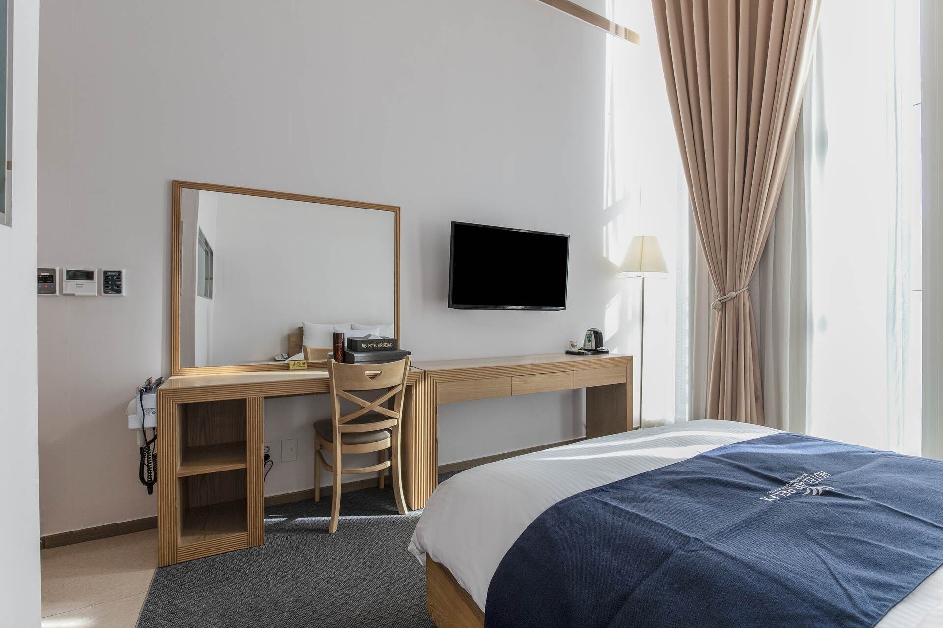 Une chambre d’hôtel comprenant un lit, un bureau avec une chaise, une télévision, un miroir et une fenêtre avec des rideaux.