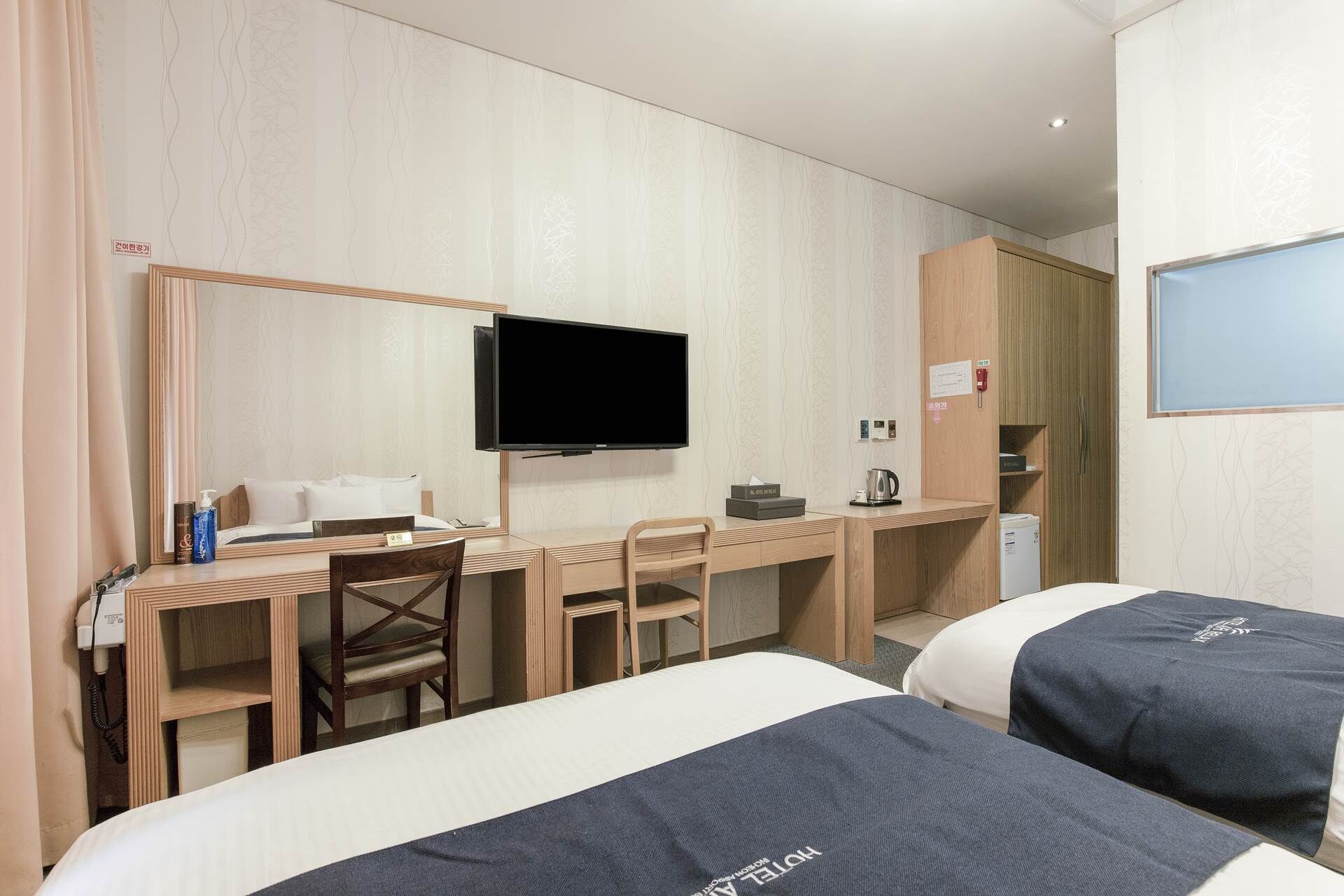 A hotel room with a bed, a desk with a chair, a television, and a wardrobe.