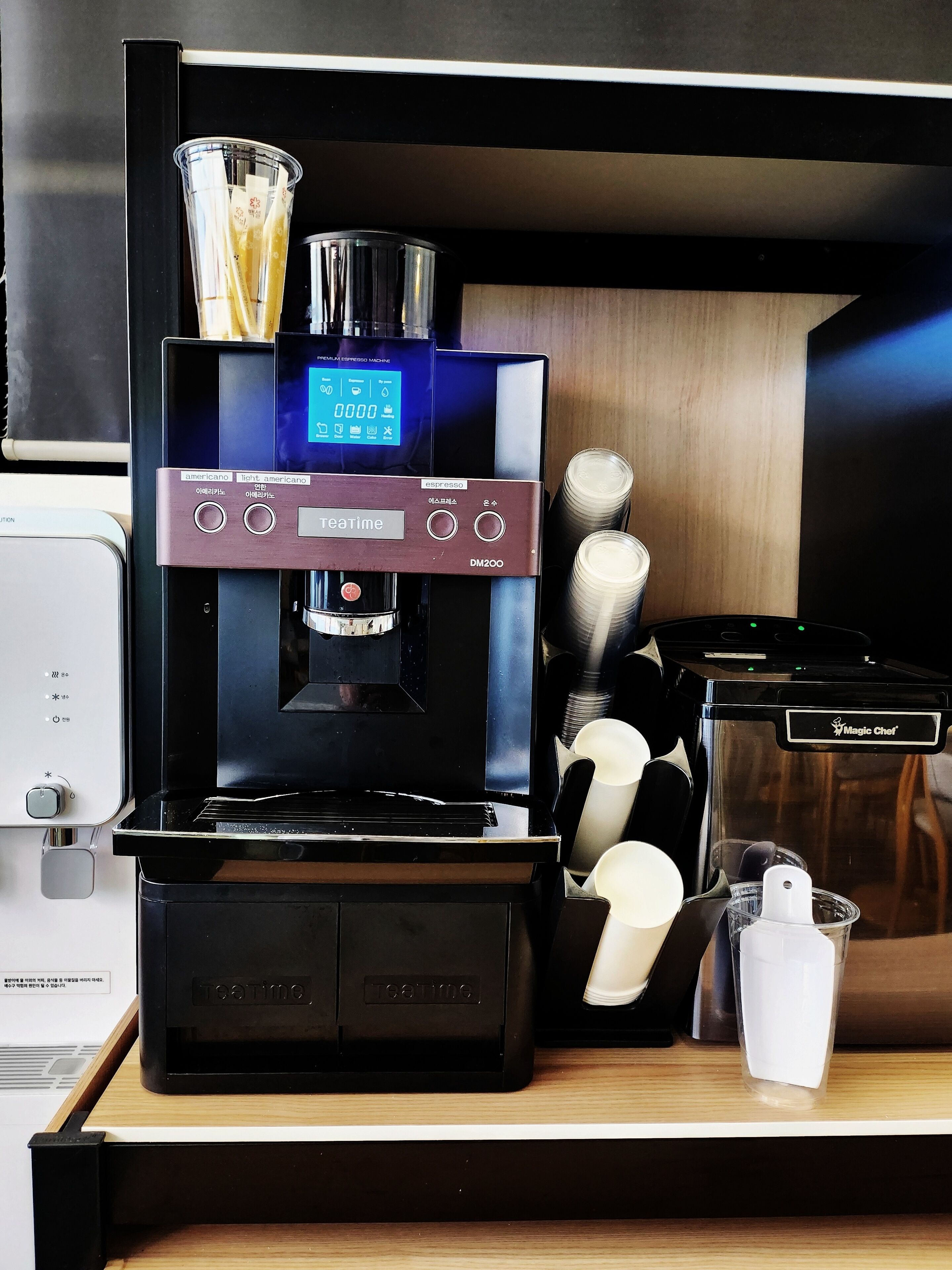A Teatime espresso machine with a digital display, coffee cups, and a Magic Chef food processor on a wooden counter.