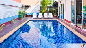 Una piscina con lettini e piante in vaso, circondata da un edificio con facciata rossa e bianca.