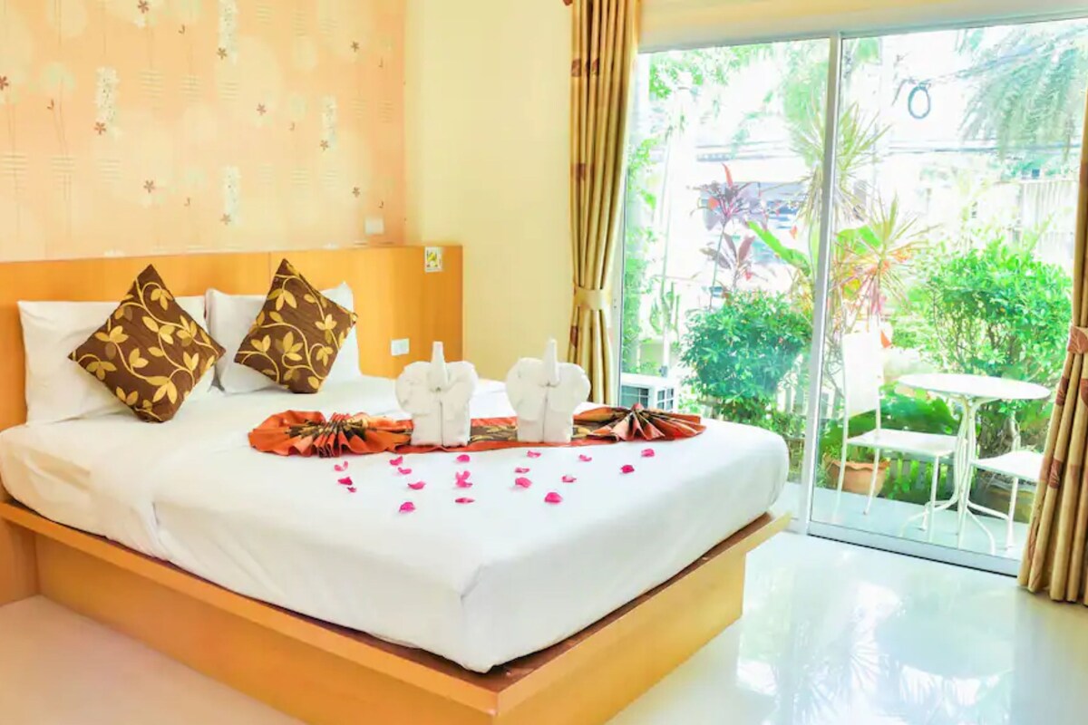 A hotel room with a bed, pillows, a bouquet of flowers, and a view of the outdoors.