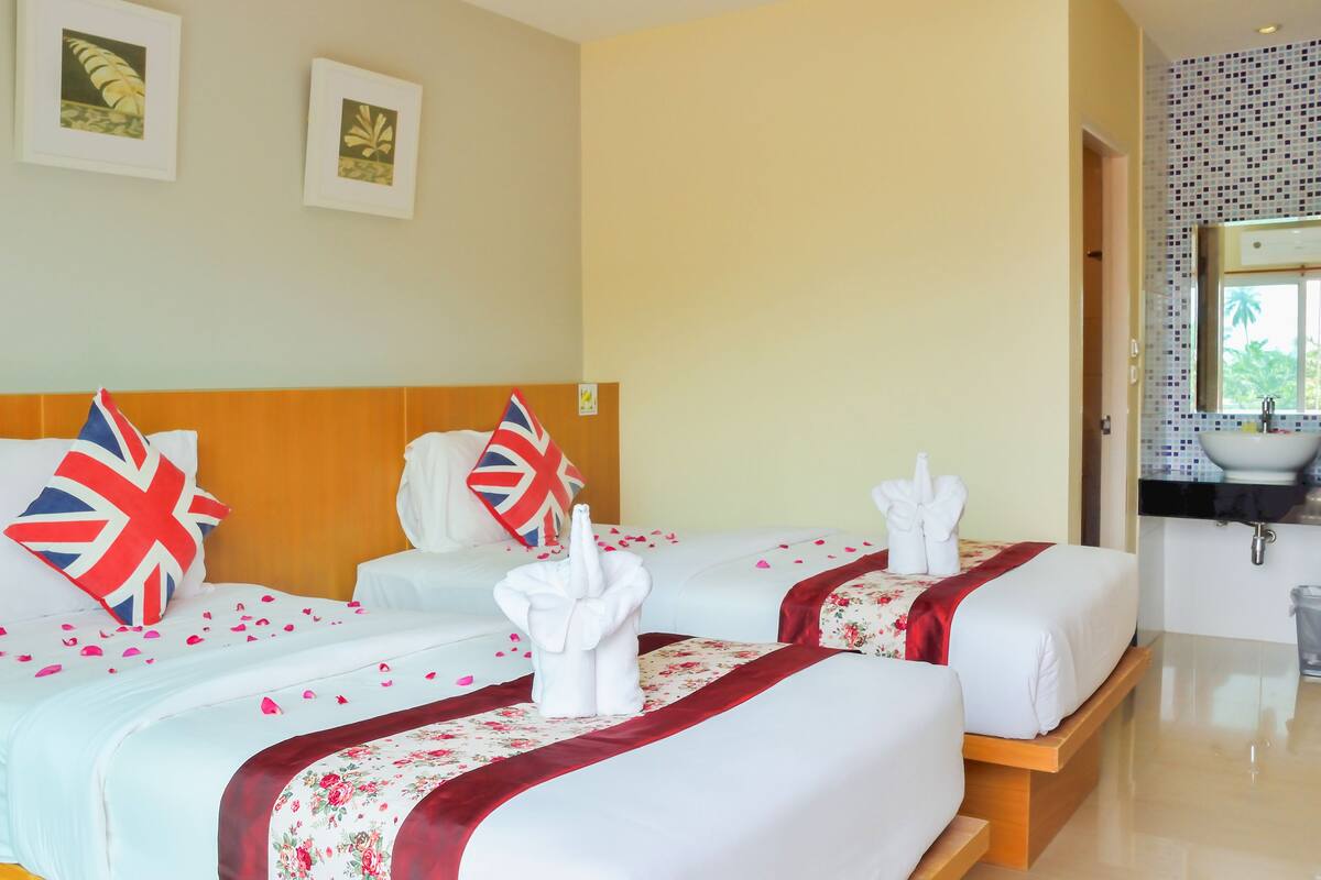 Habitación de hotel con dos camas, cada una con colcha roja y blanca de motivos florales, almohadas con diseño de la bandera del Reino Unido y un arreglo de toallas blancas.