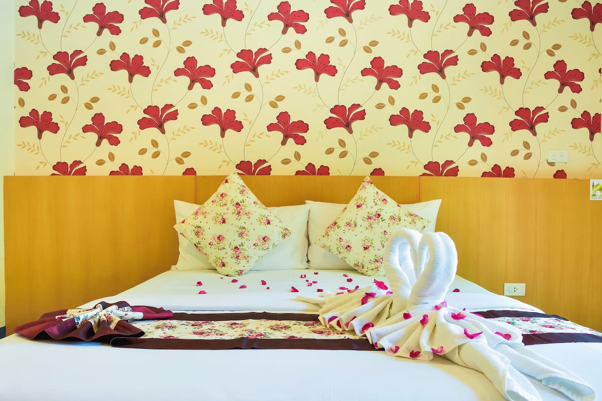 Una habitación de hotel con papel tapiz floral, un cabecero de madera y una cama con almohadas y una toalla estampadas con motivos florales.