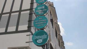 A building with circular signs indicating amenities such as a cafe, quality bed, wifi, hot shower, laundrette, and LCD TV. - Snooze Too (Brinchang)