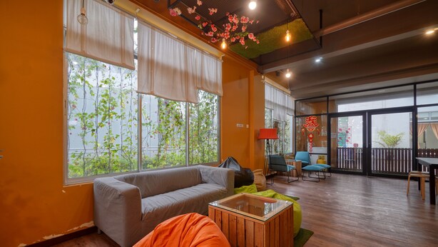 A modern living room with a sofa, bean bag, and coffee table, large windows with curtains, and a balcony with outdoor furniture. - Snooze Too (Brinchang)