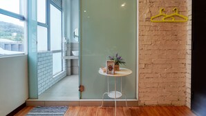 A modern hotel room with a sliding glass door leading to a balcony, a small round table with a plant and a book, and a brick wall with a yellow hanger. - Snooze Too (Brinchang)