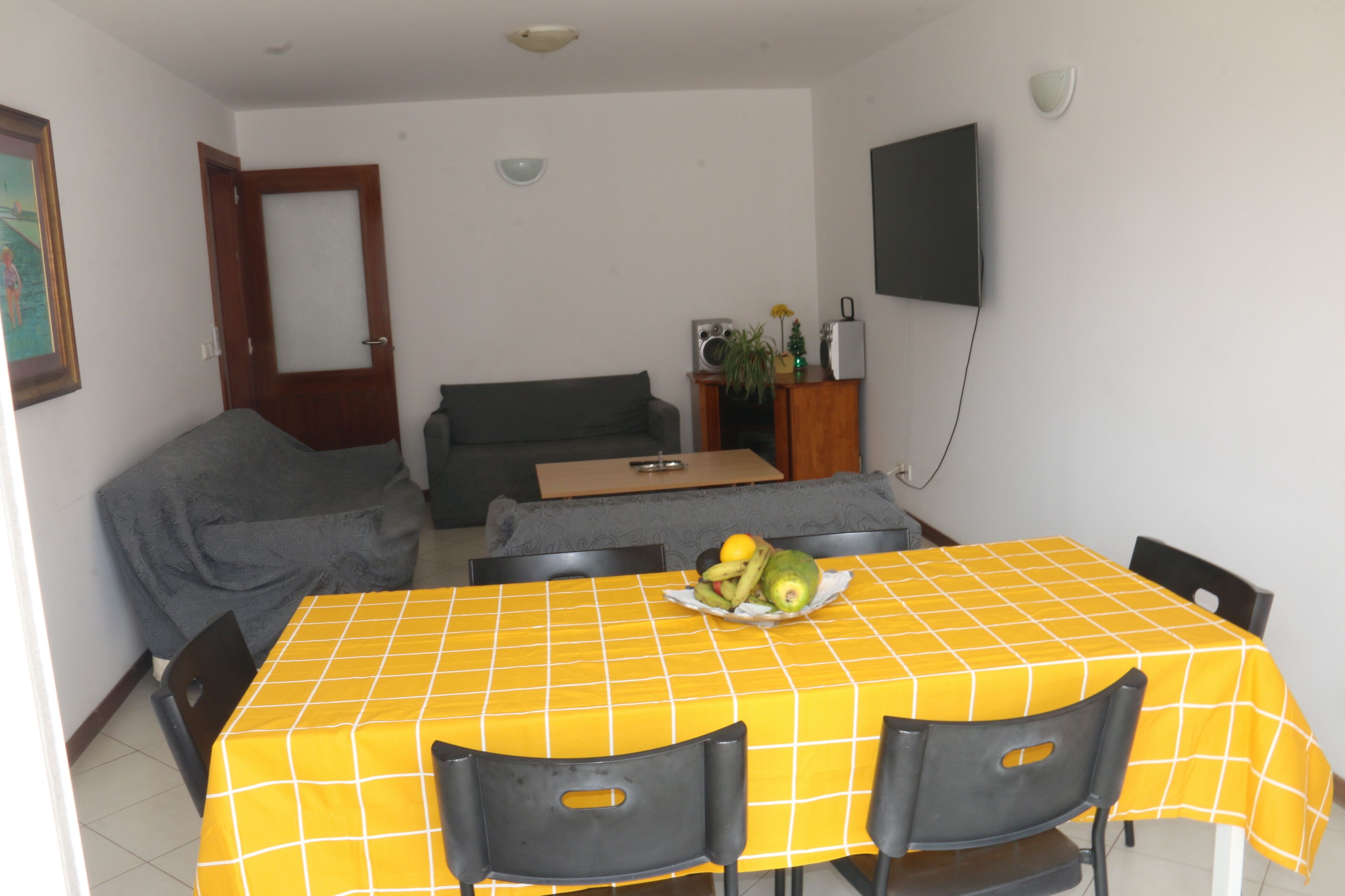 Un comedor con mantel a cuadros amarillos, un frutero y sillas negras.