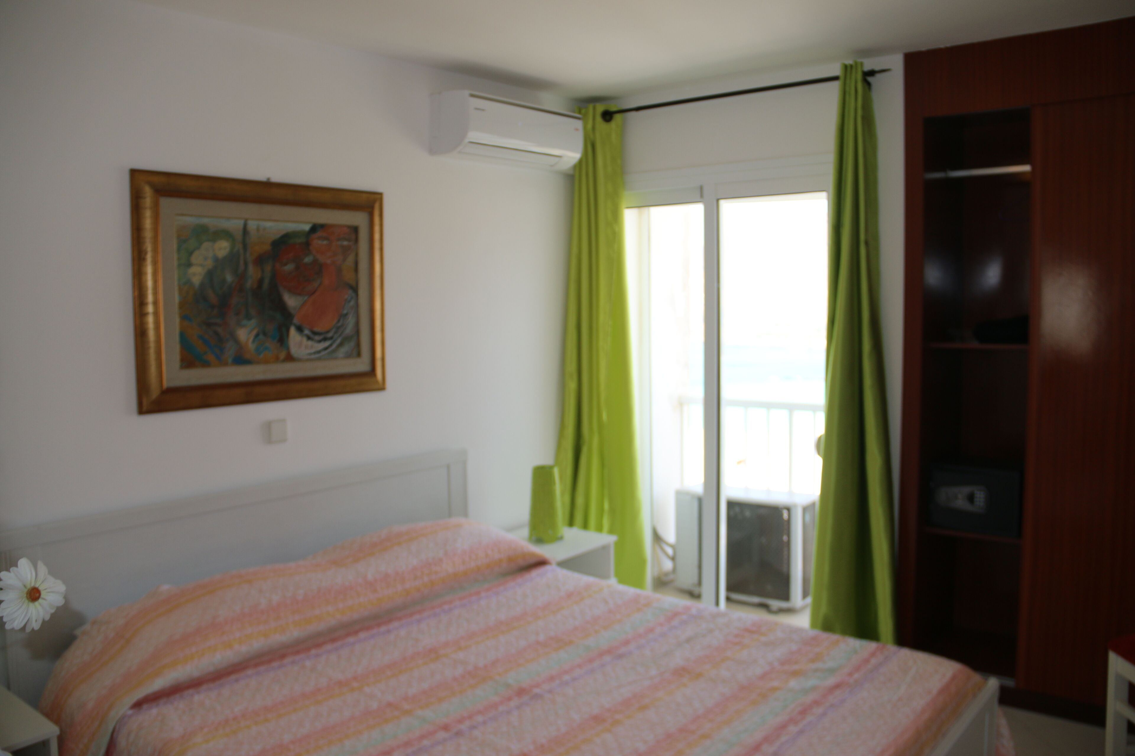 A bedroom with a bed, a painting on the wall, and a green curtain.