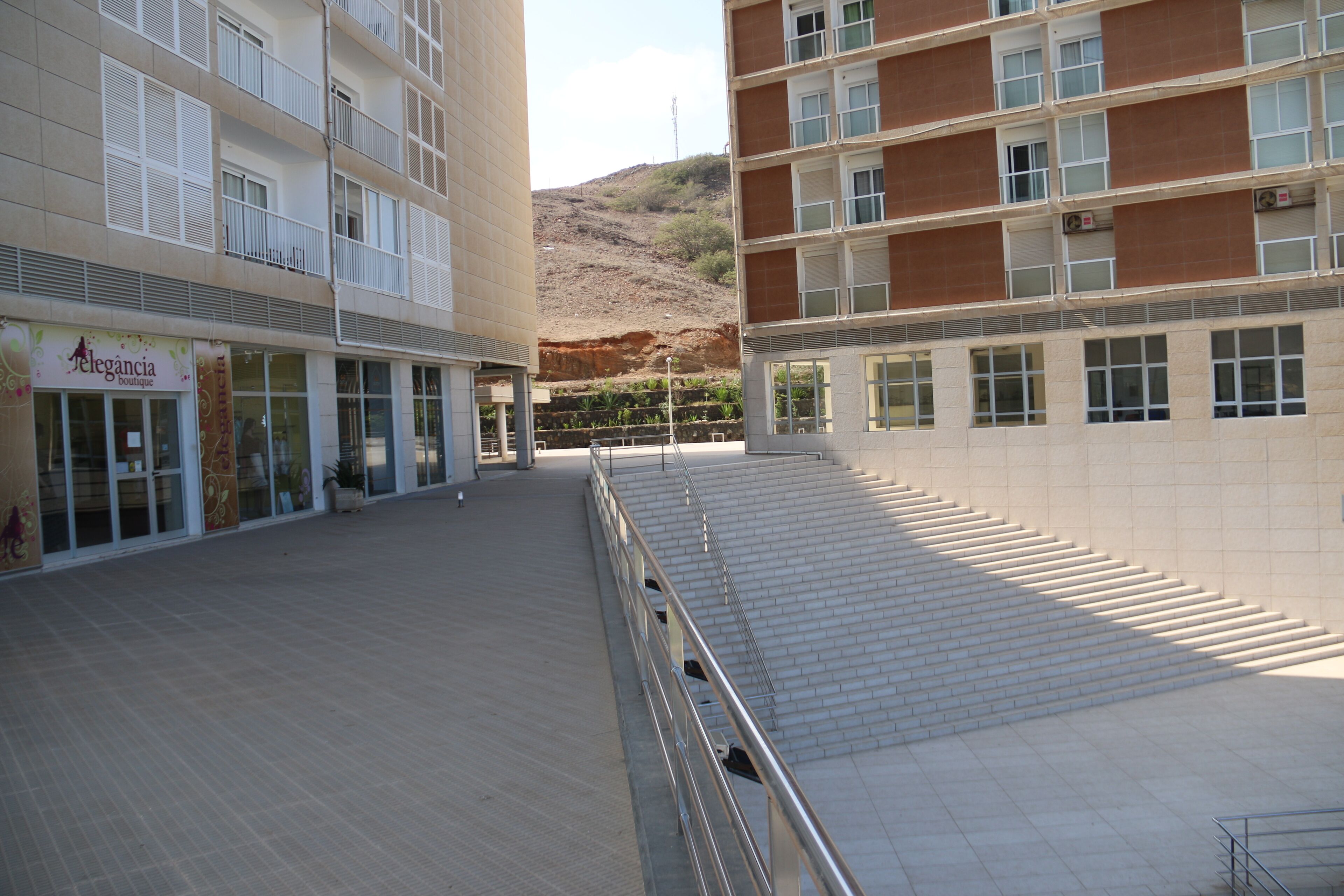 A building with a boutique on the ground floor, a staircase leading to an upper level, and a hillside in the background.