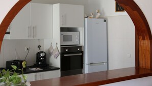 A kitchen with white cabinets, a microwave, a refrigerator, and a wooden countertop. - Complexo Multiuso Copacabana (São Vicente)