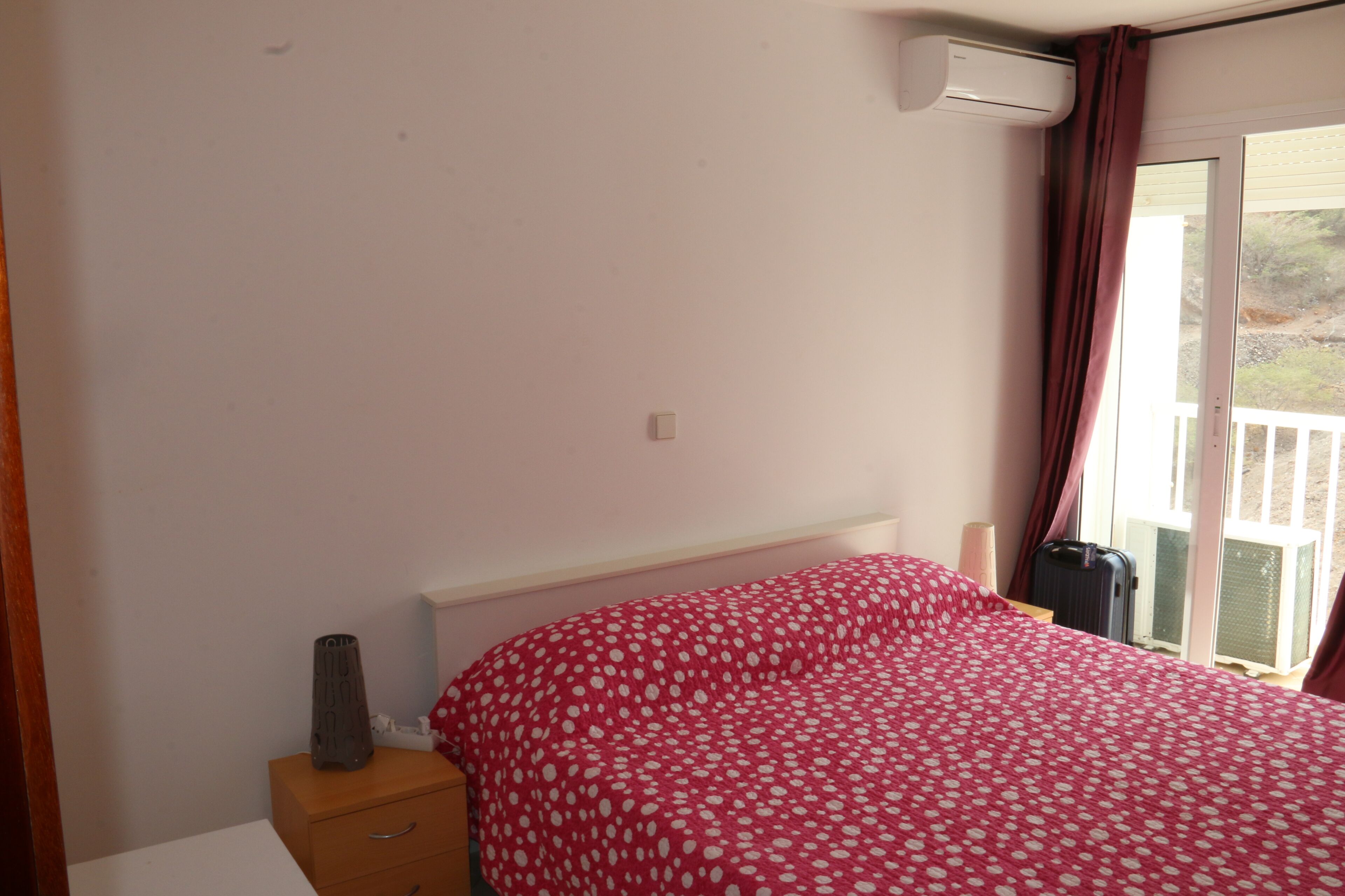A bedroom with a bed, a dresser, an air conditioning unit, and a window with curtains.