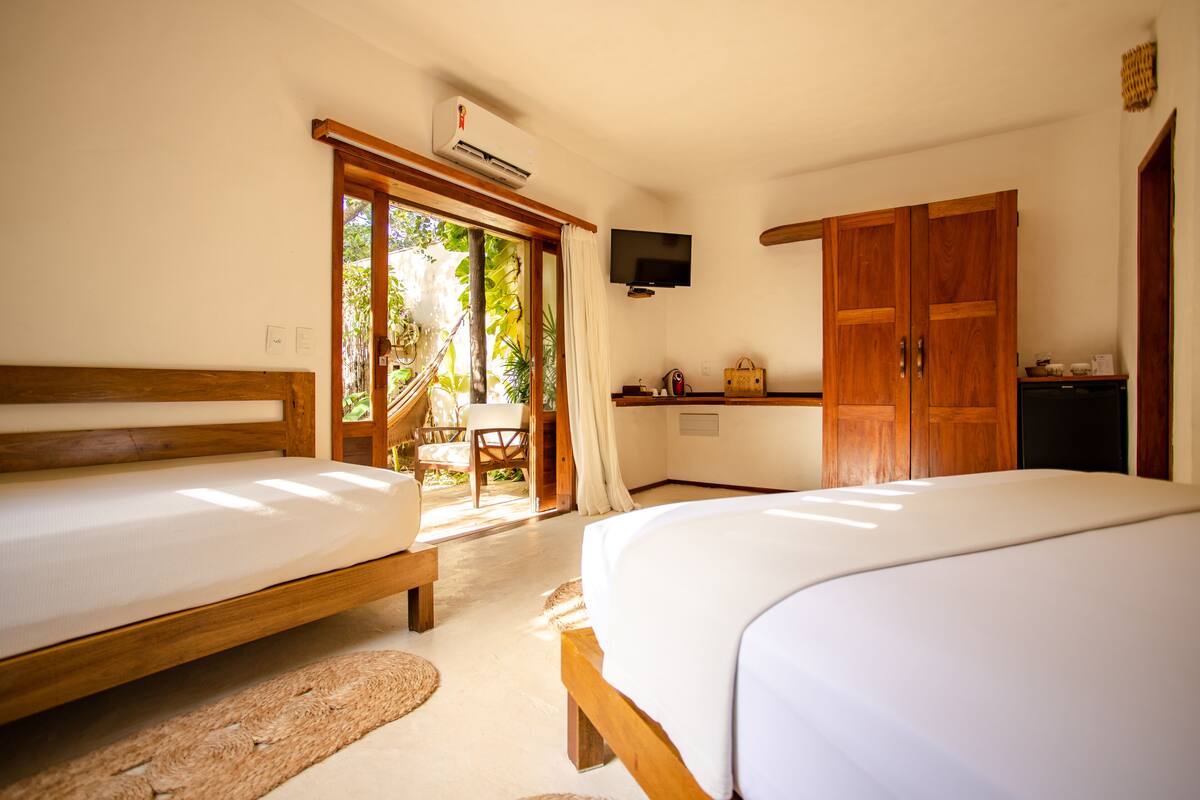 A hotel room with two beds, a TV, a wooden wardrobe, and a small kitchenette.