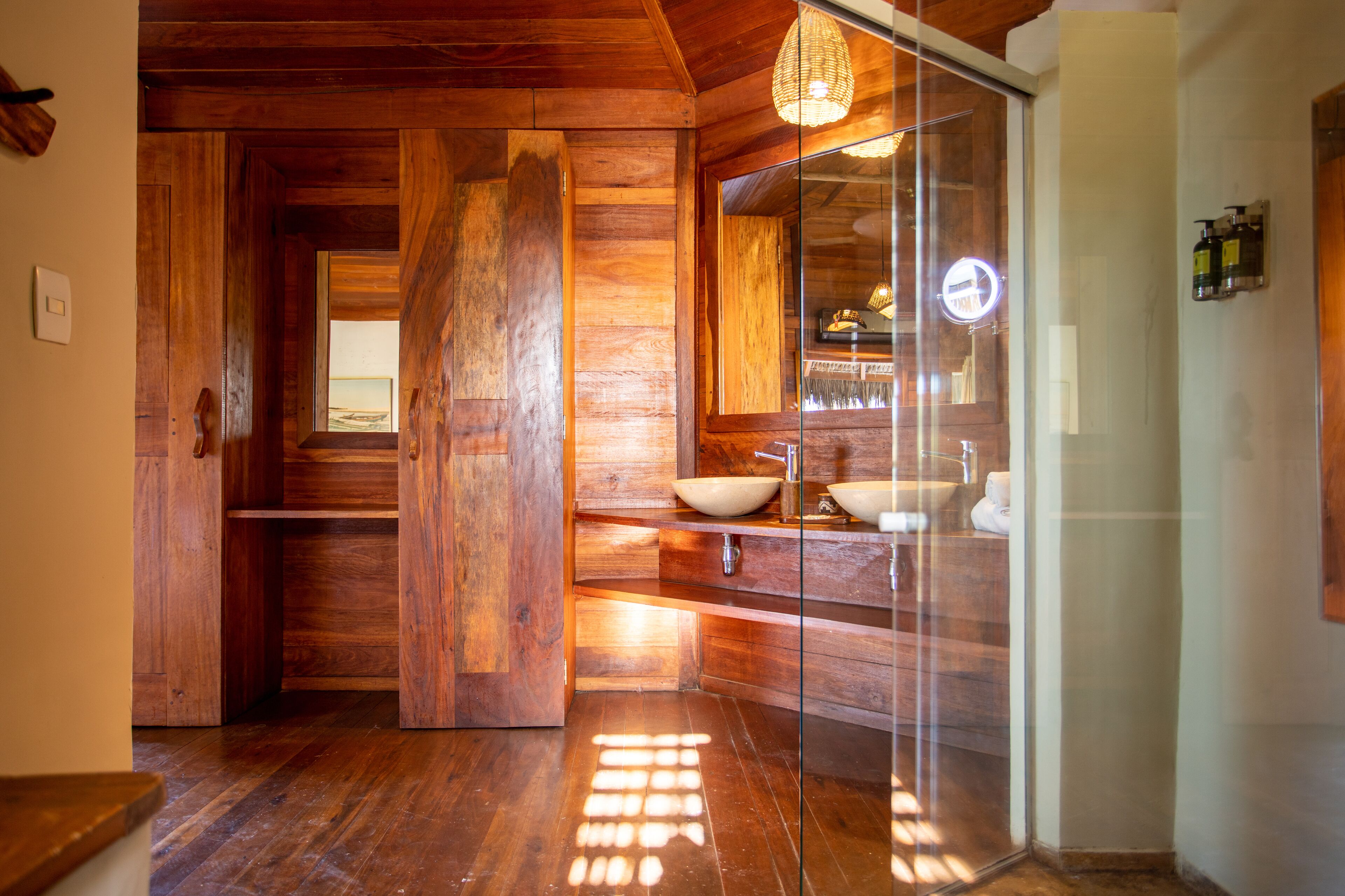 Interior de madera con cabina de ducha de vidrio, suelo de madera y lavamanos a la vista.